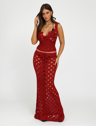 A woman is posing against a plain white background, wearing the Cherry Red Kincade Skirt from Tiger Mist. The top, a red crochet matching piece, is sleeveless and features a deep neckline. The long skirt flows gracefully to her feet with intricate patterns. She has long hair and minimal accessories for a chic look.