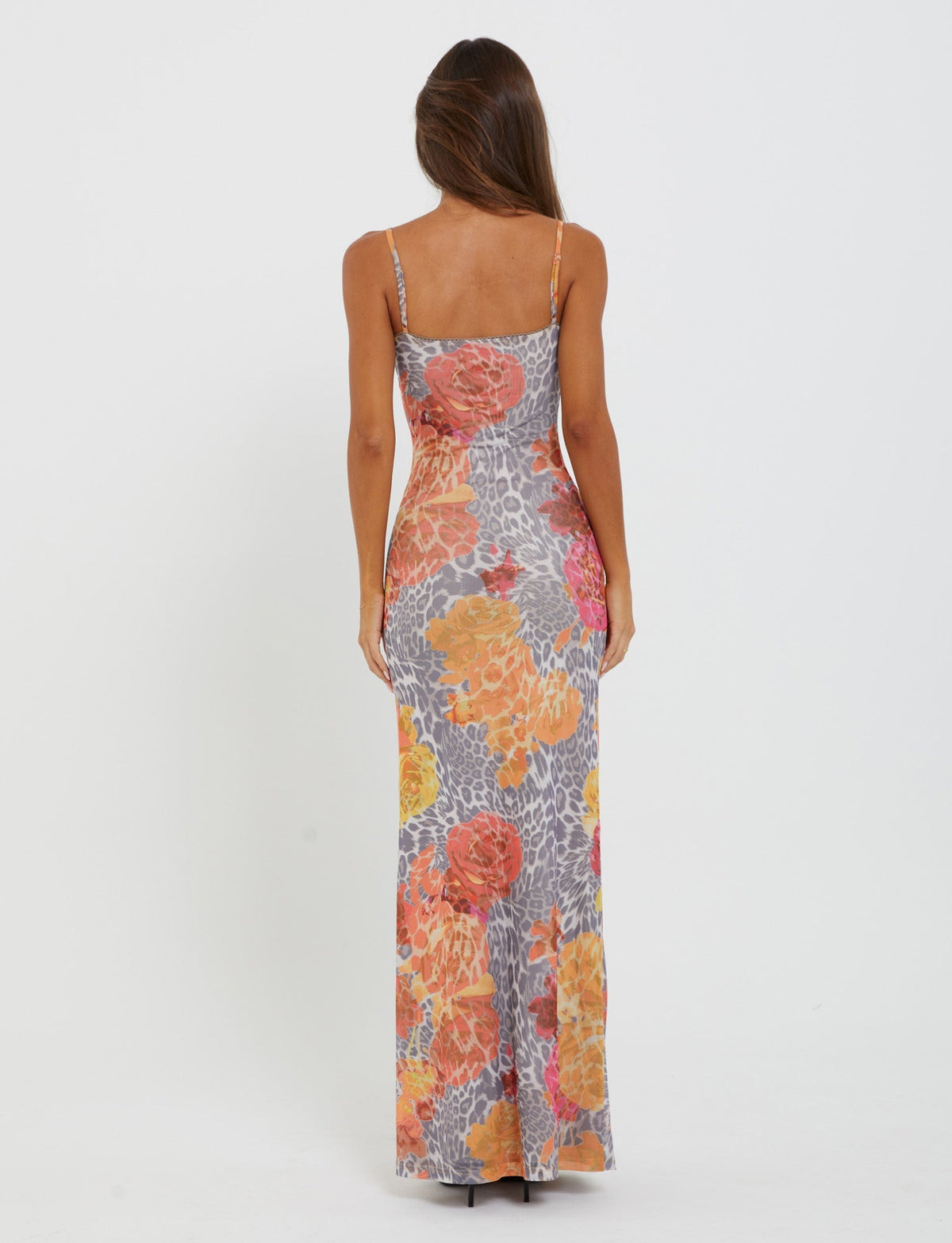 With their back to the camera, a person with long brown hair wears the JULIANNA DRESS from TIGERMIST, a floor-length, form-fitting dress adorned with thin straps and a vibrant orange leopard pattern.
