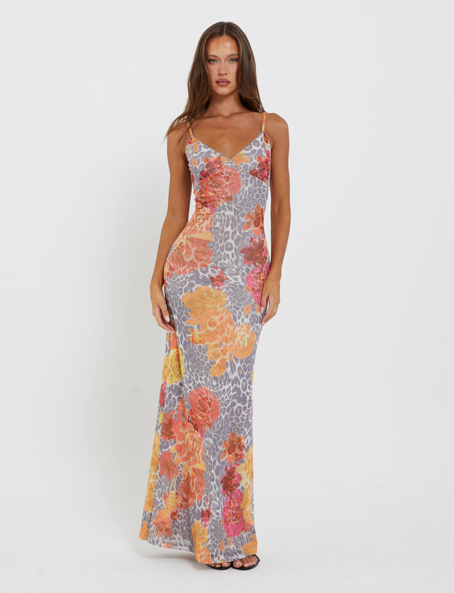 A woman stands against a plain white background, wearing the JULIANNA DRESS - MULTI : LEOPARD : ORANGE LEOPARD from TIGERMIST. This long, form-fitting dress features thin straps and a V-neckline adorned with a colorful floral and animal print pattern. She has long, straight hair and gazes directly at the camera with a neutral expression.