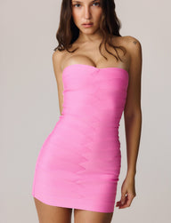 A woman with long brown hair wears the TIGERMIST NIYA BANDAGE MINI DRESS in pink, featuring a strapless sweetheart neckline and a bodycon fit that accentuates her figure. She stands facing forward against a plain light background with a neutral expression.