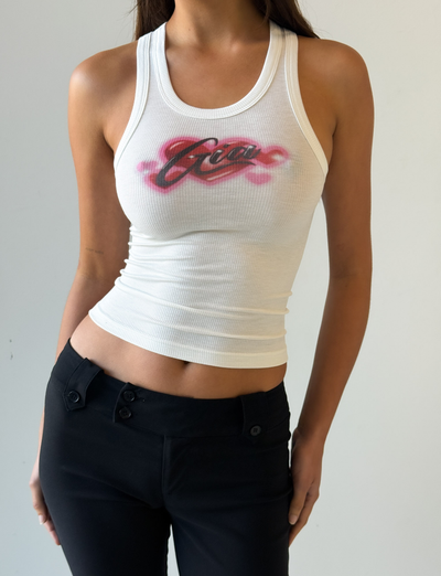 A person wears the CL - PENELOPE TANK by Tiger Mist, a fitted white ribbed top with red and black graffiti-style “Gia” text, paired with black pants against a plain light background.