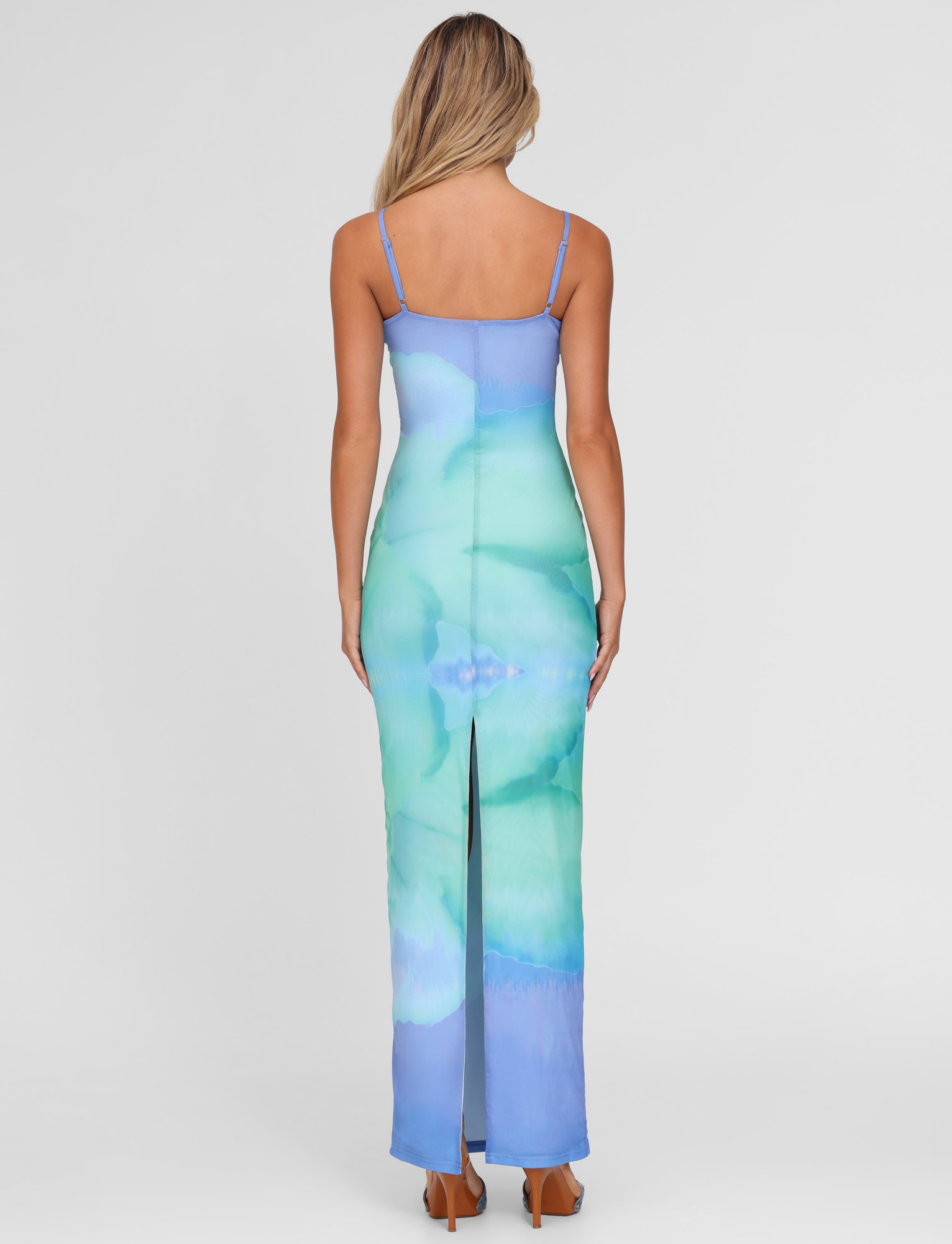 A woman with long blonde hair models the TIGERMIST ARDON MAXI DRESS in Blue Hibiscus Macro Floral, featuring thin straps and a back slit, standing against a plain white background with her back to the camera.