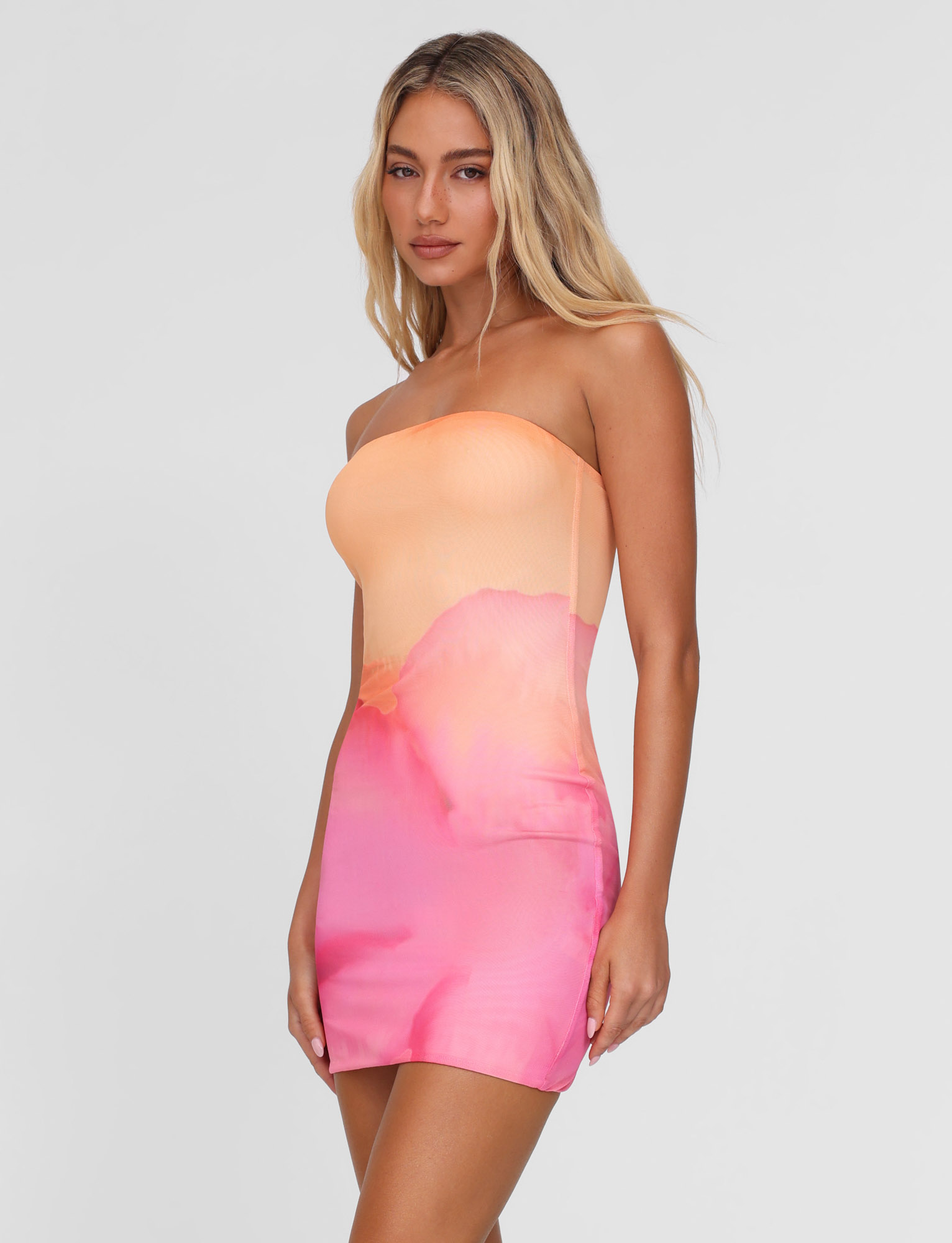 A woman with long blonde hair models the TIGERMIST CHER MINI DRESS in Macro Floral Pink Hibiscus, a strapless bandeau bodycon style, against a plain white background.