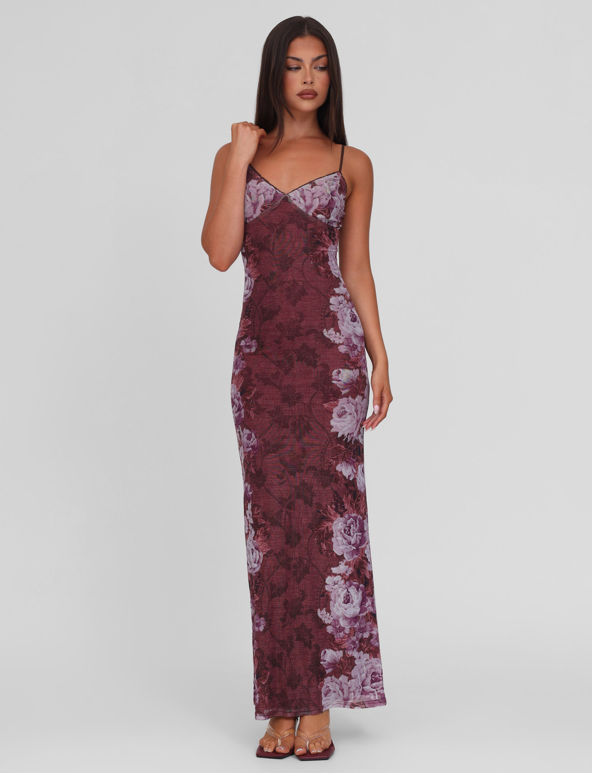 A woman with long, straight dark hair wears the TIGERMIST JULIANNA DRESS - MULTI: FLORAL: ROSE STRIPE, a sleeveless, floor-length dress with thin straps and a floral stripe print, standing against a plain background in open-toed heels.