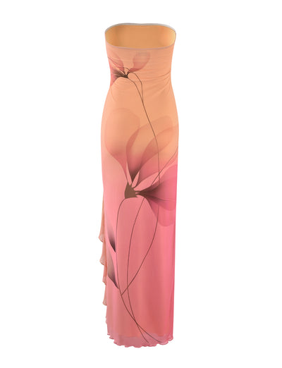 The Theo Maxi Dress from TigerMist is a strapless, floor-length gown with a fitted bodice in a gradient of soft peach to pink hues. Featuring a delicate, abstract floral design and a subtle side slit, this dress exudes a flowing and elegant appearance.