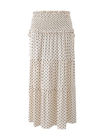 The DENALI MAXI SKIRT - CREAM DOT by TIGERMIST features a cream base with black polka dots, a smocked waistband, and a tiered silhouette—an effortlessly elegant maxi skirt for any occasion.