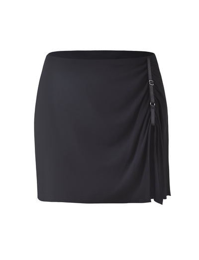 The ALANI Skirt - Black by TIGERMIST is a high-waisted mini skirt with a slight sheen. It features decorative ruching on the right side, adorned with three small silver buckle accents. The straight hemline falls above the knees, giving this skirt a fitted and elegant appearance.