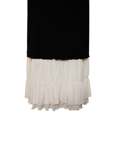 The KACIE DRESS - BLACK from TIGERMIST is a two-tone maxi skirt with a black upper section and a white, ruffled lower section. The layered white fabric extends below the black, creating an eye-catching contrast. The skirt has a straight silhouette with no visible patterns or embellishments.