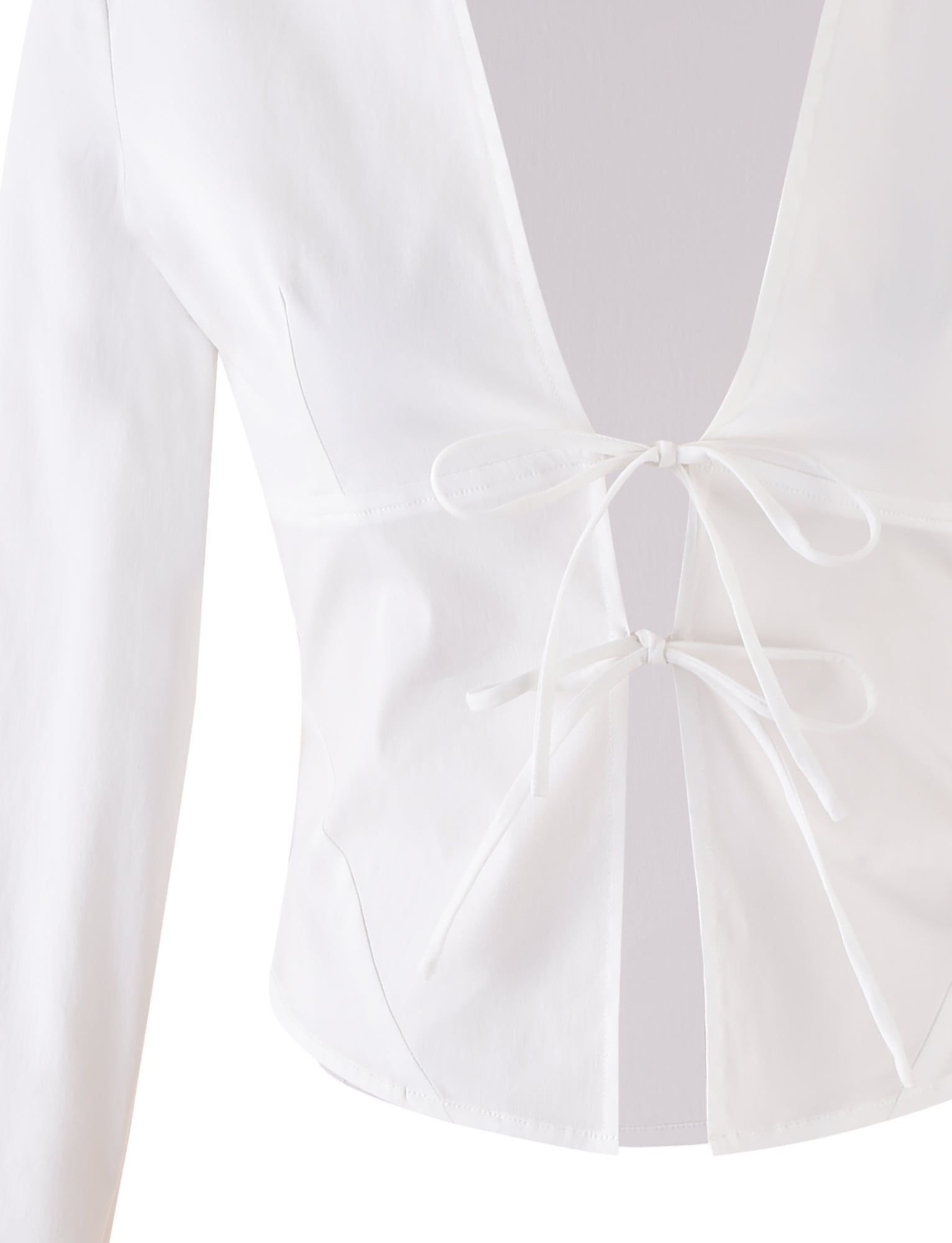 The ELVA SHIRT - WHITE by TIGERMIST is a white, long-sleeved top featuring a deep V-neck and two front ties. It showcases minimalist design elements with a tailored, sleek fit and is displayed on a light gray background.