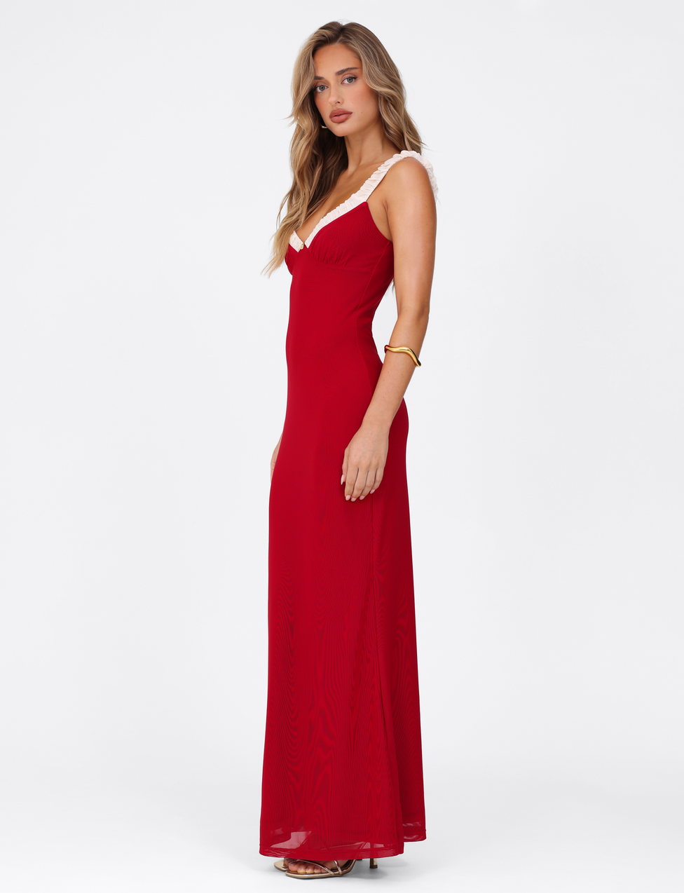 A woman with long, wavy blonde hair models the TIGERMIST AMARAN MAXI DRESS - RED : BURGUNDY, featuring white strap trim and an elegant bodycon fit. She wears gold bracelets and heeled sandals against a plain white background.