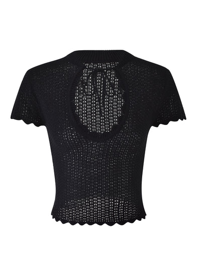 The TEREZA TOP - BLACK from TIGERMIST is a black knitted short-sleeve top featuring a tie detail at the back of the neck and a large keyhole cutout beneath it. The hem and sleeves boast wavy, scalloped edges, while the fabric features a loosely woven, airy pattern.