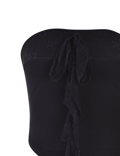 A close-up of the HARPER TOP - BLACK by TIGERMIST, showcasing its delicate lace fabric. This black strapless top features a decorative lace bow in the center of the bodice, adding an elegant touch to its simple, chic design. The intricate lace texture contrasts beautifully with the smooth main fabric.