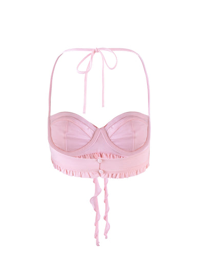 The HEAVEN TOP - PINK by TIGERMIST is a light pink halter-style bralette with padded cups and a ruffled band under the bust, featuring two buttons at the center front and ties at the back that create a bow with flowing straps.