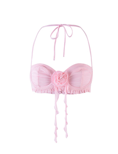 The HEAVEN TOP - PINK by TIGERMIST is a light pink, strapless bikini top with ruffles along the bottom edge. It boasts a large, decorative fabric rose at the center and has thin, adjustable ties for halter neck support, exuding classic elegance.