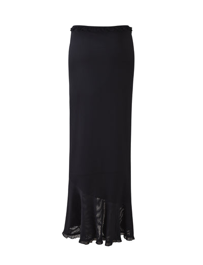 The HEAVEN MAXI SKIRT by TIGERMIST is a long, black, high-waisted skirt featuring a slightly ruffled hem. This elegant design is enhanced by a sheer, asymmetrical layer at the bottom, adding a flowing and sophisticated touch to the overall look.