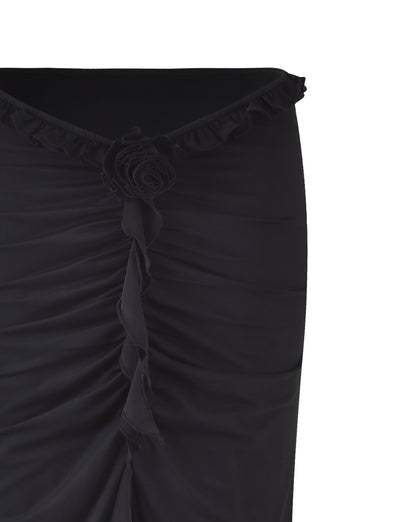 Image of the HEAVEN MAXI SKIRT - BLACK by TIGERMIST, with a close-up focus on a gathered section at the top, adorned with a ruffled edge and a decorative fabric rose in the center. The fabric appears textured and slightly ruched, suggesting a form-fitting design.
