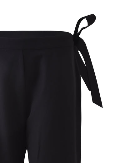 Close-up of the TRISTAN PANT from TIGERMIST, showcasing a high-waisted design with a fabric tie detail on the left side. The black pants feature a knotted bow, adding a stylish touch to the classic look.