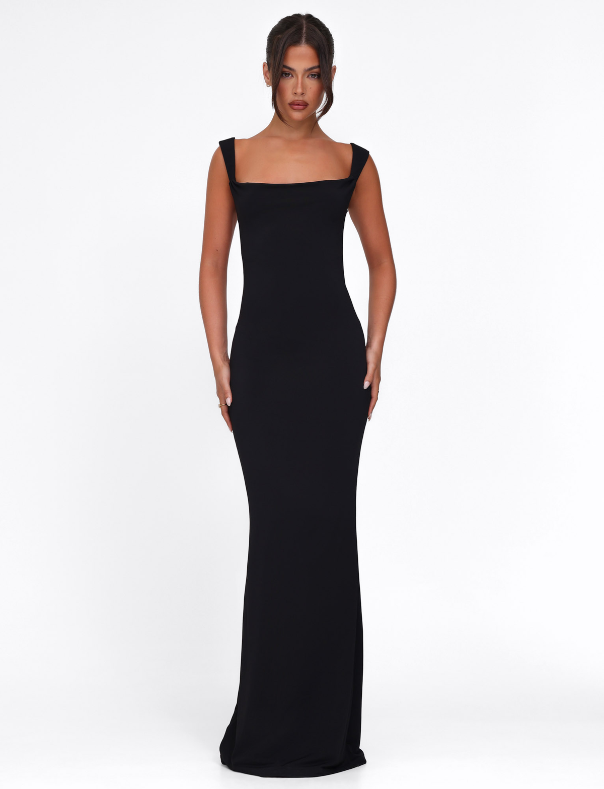 A woman stands facing forward, wearing the TIGERMIST ZITA DRESS - BLACK—a floor-length, sleeveless black bodycon maxi dress with wide straps and a straight neckline—against a plain white background.