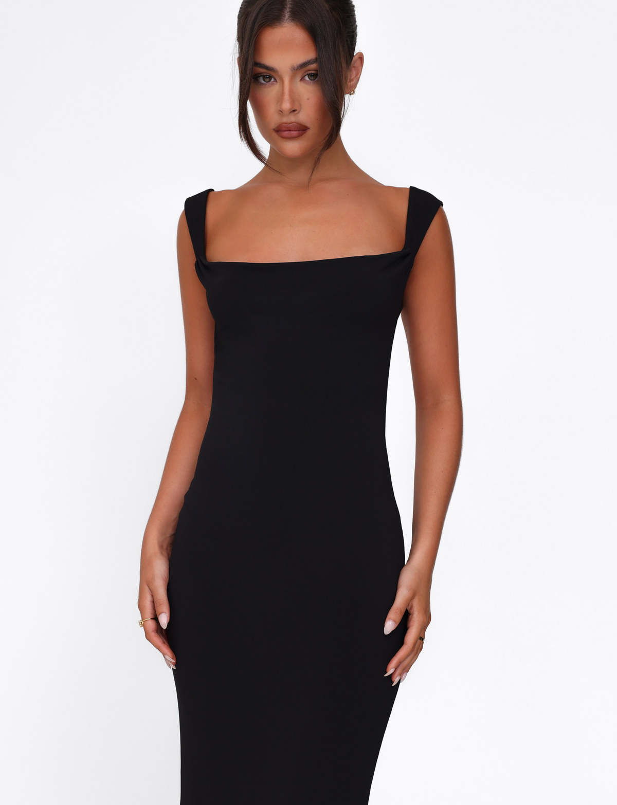 A woman with dark hair in an updo wears a fitted TIGERMIST ZITA DRESS in black, featuring a bodycon silhouette and wide shoulder straps, standing against a plain white background and looking directly at the camera.