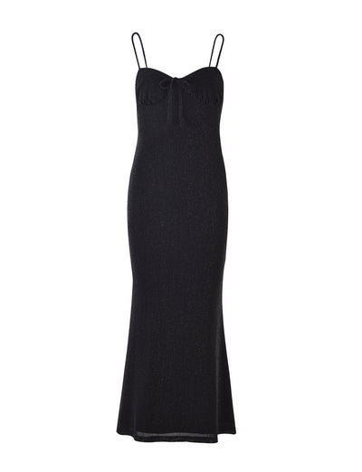The CATYA DRESS - BLACK : BLACK SHIMMER by TIGERMIST is a sleeveless, full-length evening gown featuring thin spaghetti straps and a sweetheart neckline adorned with a small bow at the center. Its form-fitting silhouette gently flares at the hem and is crafted from subtle, shimmering fabric.