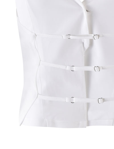 The JAYLIN VEST - WHITE by TIGERMIST is a white garment resembling a straitjacket, featuring multiple horizontal straps and buckles across the front and primarily composed of smooth fabric. The close-up image focuses on the midsection, highlighting the fastenings and overall design.
