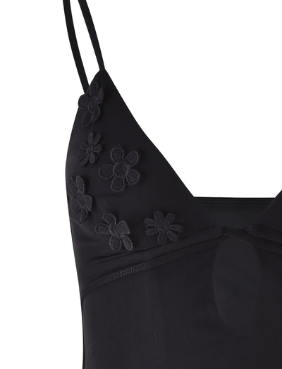 Close-up of the KATINA CAMI - BLACK from TIGERMIST. This black dress features spaghetti straps and delicate, sheer fabric adorned with embroidered flower designs on the bust area. A small keyhole cutout below the neckline adds a charming detail.