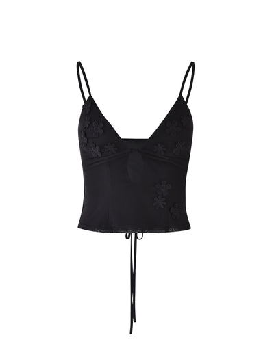 The KATINA CAMI - BLACK from TIGERMIST is a black cropped camisole with thin spaghetti straps and decorative floral embroidery. It features a low-cut V neckline, an under-bust seam, and a tie detail at the back.