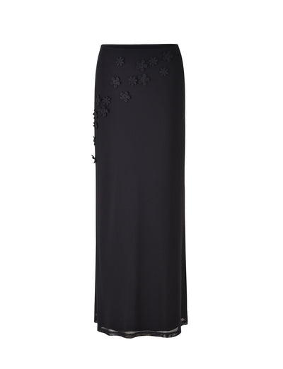 The KATINA SKIRT - BLACK by TIGERMIST is a long, elegant skirt featuring subtle, small floral embellishments scattered on the upper portion. Designed with a straight cut that reaches the ankles, it also boasts a slightly sheer hemline.