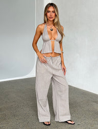 A woman stands against a plain backdrop, wearing the LAINEY PANT - GREY : STRIPE from TIGERMIST. She pairs it with a matching gray and white striped halter top. Her long blonde hair cascades down, and she accessorizes her look with a pendant necklace and bracelets. She exudes confidence, posing with one hand on her hip.