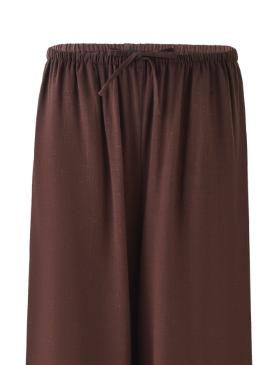 A close-up of TIGERMIST's LAINEY PANT - CHOCOLATE, mid-rise wide leg linen pants with an elastic waistband and front drawstring tie, featuring a subtle textured fabric pattern.