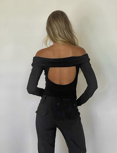 A person with long, blonde hair is standing with their back to the camera, wearing the INDIANA TOP - BLACK from TIGERMIST featuring a large cutout on the back and high-waisted black pants. The background is plain and white.
