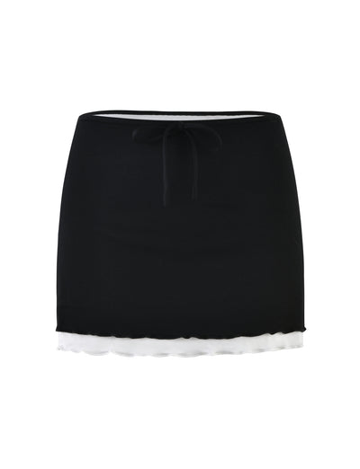 The ADAIR SKIRT - BLACK by TIGERMIST features a black mini skirt with a white underskirt peeking out at the bottom, creating a stylish layered look. The design is simple yet chic, boasting a waistband and a drawstring tie in the front.