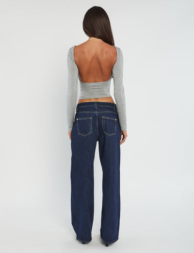 A person with long brown hair is shown from the back, dressed in a chic TIGERMIST outfit. They are wearing the QUINNELL TOP - GREY, a long-sleeved, backless top paired with dark blue wide-leg jeans. The background is plain white.