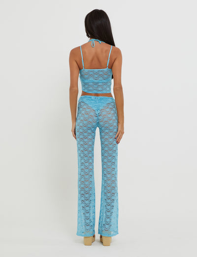 A person with long dark hair is standing with their back to the camera, wearing a fashionable KAELANI TWO-PIECE TOP in ice blue from TIGERMIST. The ensemble features a sleeveless crop top and flared pants. They are poised on light-colored, high-platform shoes against a plain white background.