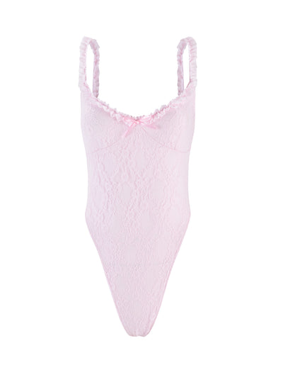 The DEJA BODYSUIT - PASTEL PINK by TIGERMIST features thin ruffled shoulder straps, a small satin bow at the center of the neckline, scalloped trim at the bust, and a high-cut leg design. The pink lace bodysuit showcases a delicate floral pattern for an intricate and delicate appearance.