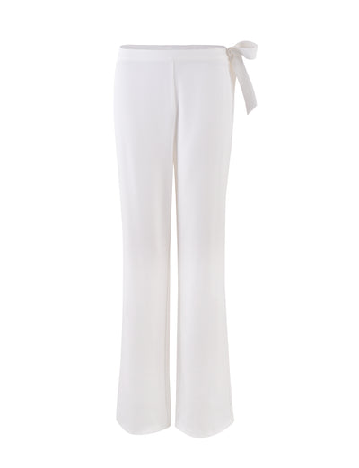 The TRISTAN PANT — WHITE by TIGERMIST features high-waisted, wide-leg trousers with a tie-waist detail on the right side. These trousers have a smooth, elegant appearance designed to offer a relaxed yet chic look.