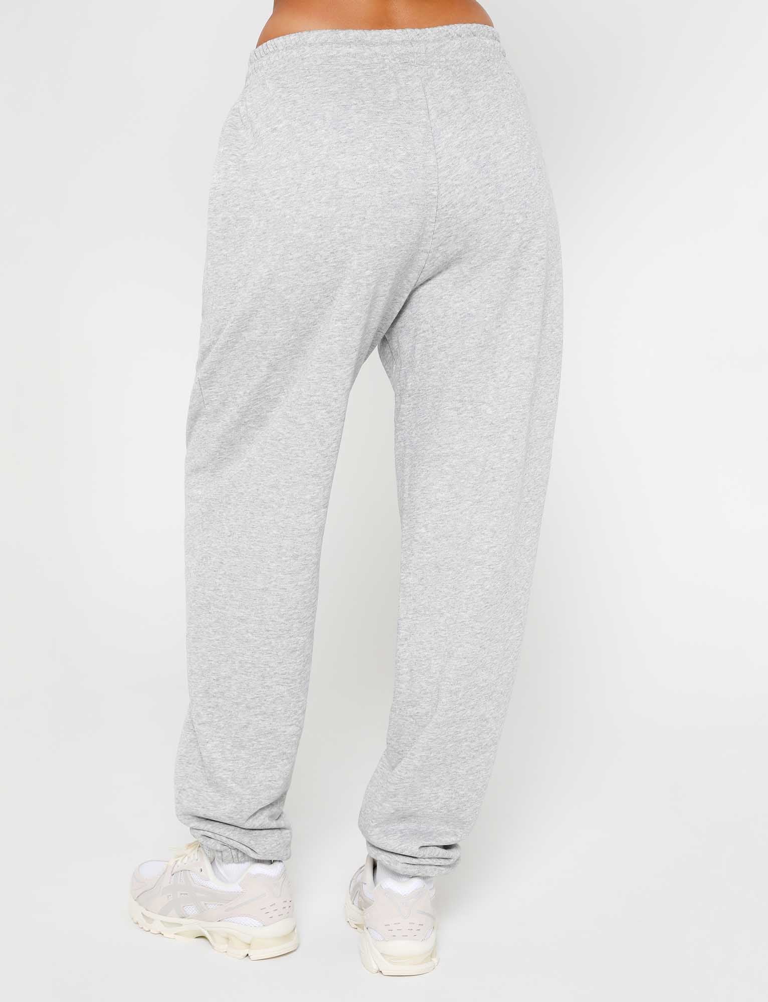 The image shows a person from the waist down wearing the ALISH PANT - GREY : GREY MARLE and white sneakers, likely from the trendy brand TIGERMIST. The person is standing with their back to the camera, feet slightly apart against a plain white background.