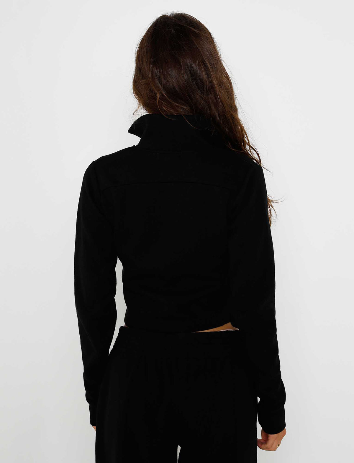 A person with long, wavy hair is facing away from the camera, wearing the VERDA JACKET - BLACK and black pants from TIGERMIST. Their back is visible against a plain white background.