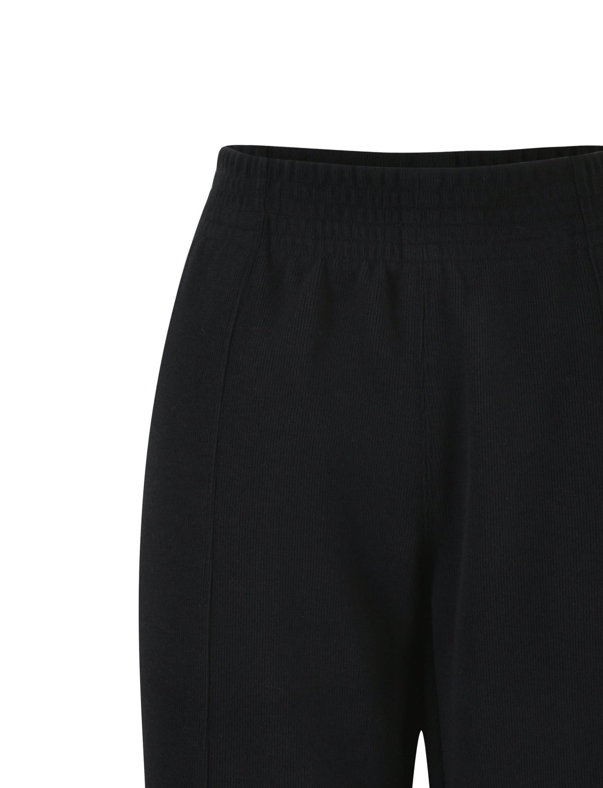 A close-up image of the VERDA PANT - BLACK by TIGERMIST. The pants feature an elastic waistband with visible stitching and a smooth, seamless front. The fabric appears to be soft and slightly stretchy. The image focuses on the upper portion of the pants, ending just above the knees.