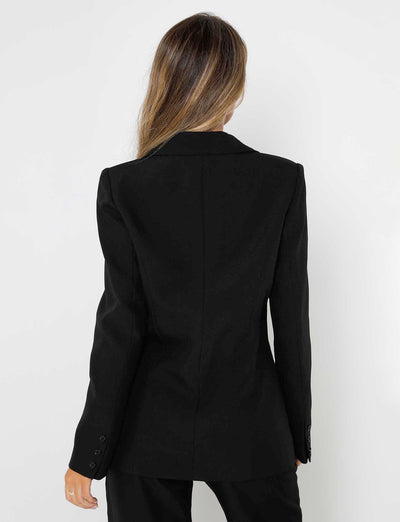 A person with long hair, seen from behind, is wearing the professional MARJORIE JACKET - BLACK from TIGERMIST and black pants. They are standing against a plain light-colored background.