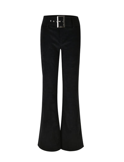 A woman with long dark hair wears a black sleeveless crop top and the ANEYA PANT - BLACK CORD, which features a low-rise waist and large square buckles. The flared silhouette accentuates her figure as she stands confidently in black sunglasses and open-toe heels against a plain white background.