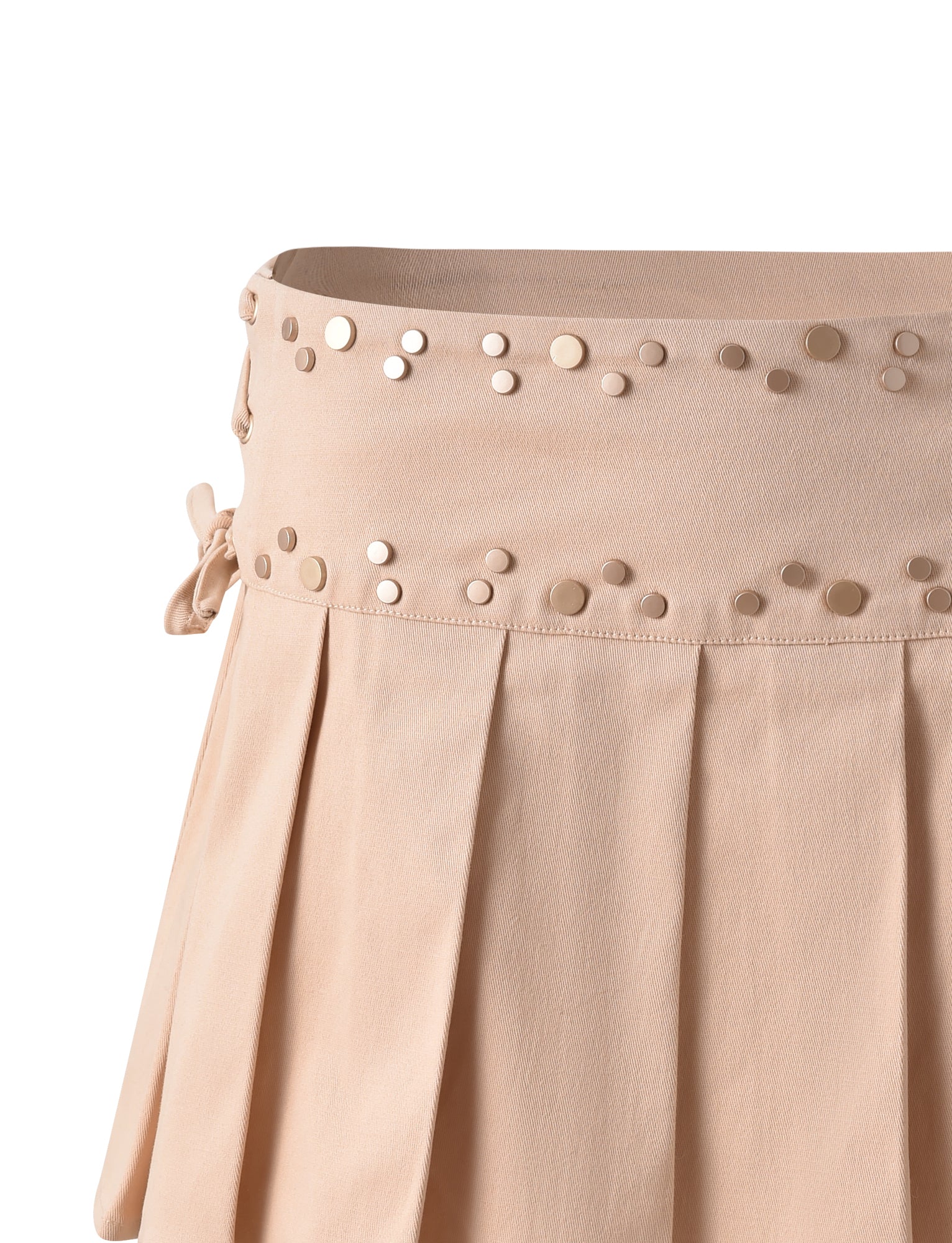 A close-up of the NOVALIE SKIRT - BEIGE : TAN by TIGERMIST featuring a high-waisted design and a wide waistband adorned with gold stud embellishments. The skirt has pleats that cascade from the waistband to the hem, with a small bow detail on the side.
