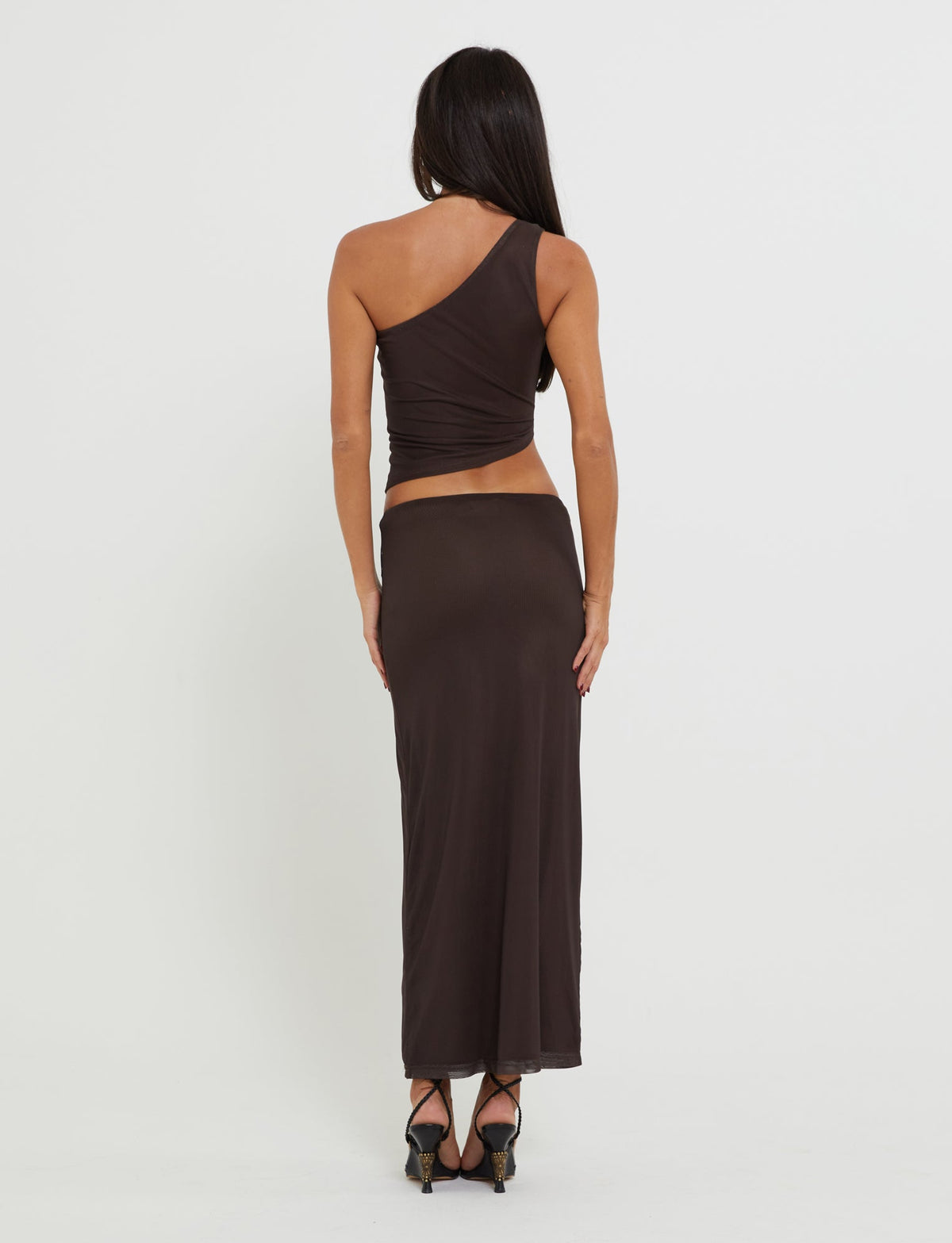 A person with long, dark hair stands facing away, wearing a sleek, form-fitting TIGERMIST brown one-shoulder top paired with the matching NANCI SKIRT - BROWN : BUTTERFLY. They also sport high-heeled shoes against a plain white background.