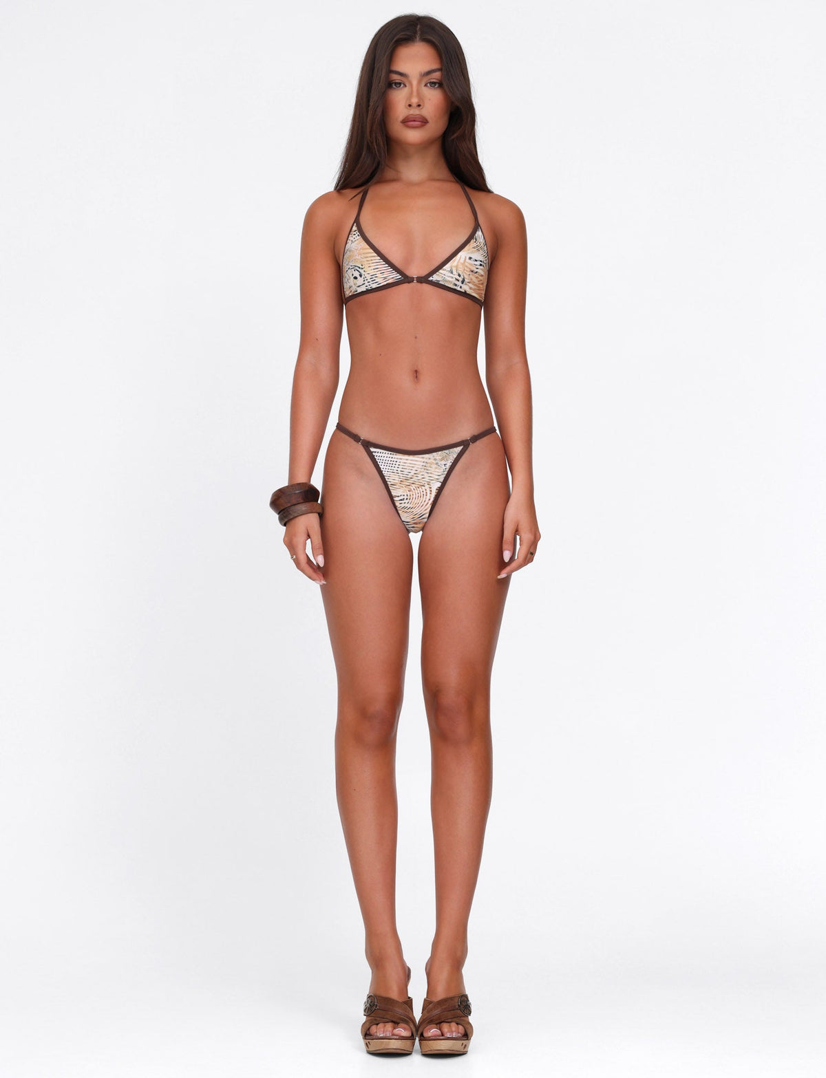 A woman with long, straight hair and a neutral expression faces forward against a white background, wearing the TIGERMIST DIANA BIKINI TOP in Animal Marble and chunky brown bangles on one arm.