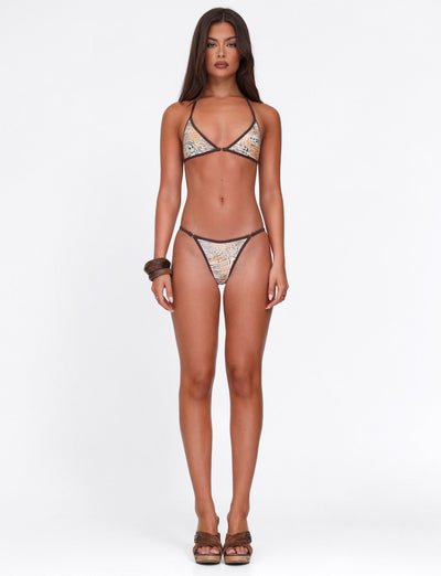 A woman with long, straight hair and a neutral expression faces forward against a white background, wearing the TIGERMIST DIANA BIKINI TOP in Animal Marble and chunky brown bangles on one arm.