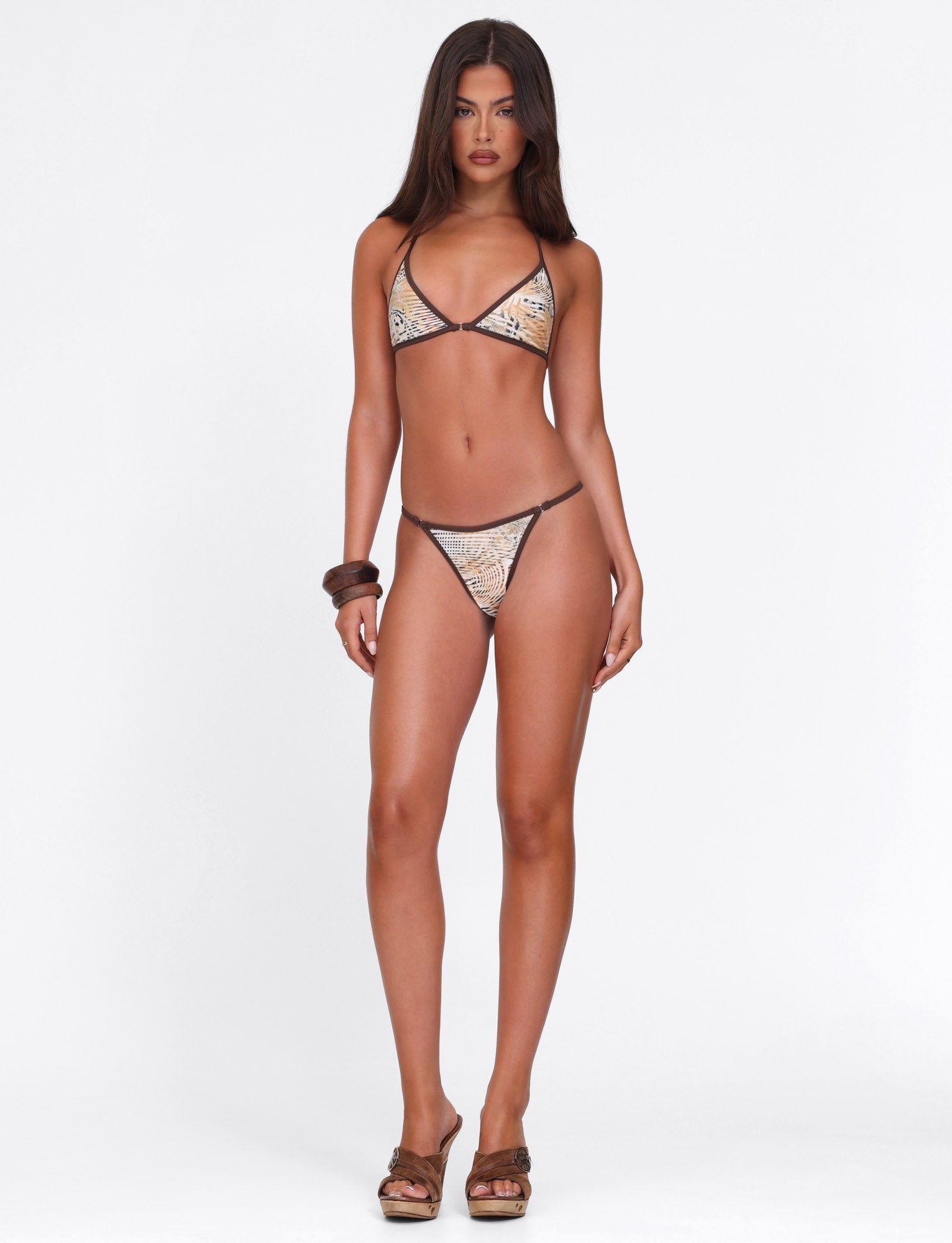 A woman with long brown hair stands against a white background, wearing the TIGERMIST DIANA BIKINI TOP in Animal Marble, along with brown wedge sandals and a bangle. She looks directly at the camera with a neutral expression.
