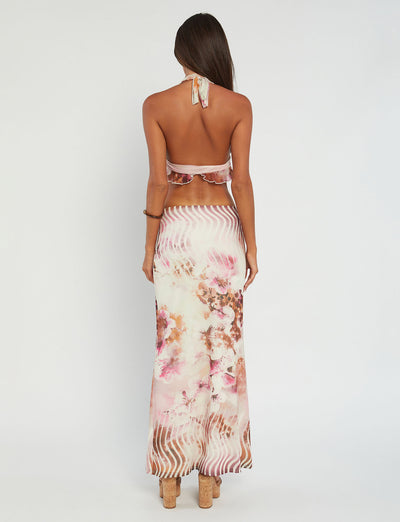 A woman stands with her back to the camera, showcasing the TIGERMIST Macey Top - Multi : Floral and a long, flowy skirt adorned with a floral pattern in shades of pink, white, and brown. Her long, dark hair is loose as she stands on a neutral background.