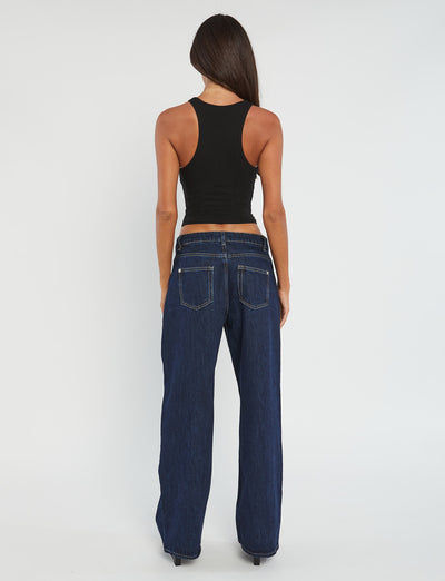 A woman with long dark hair stands with her back to the camera, dressed in a sleeveless SOMMER TANK - BLACK and dark blue wide-leg jeans from TIGERMIST. The background is plain white.