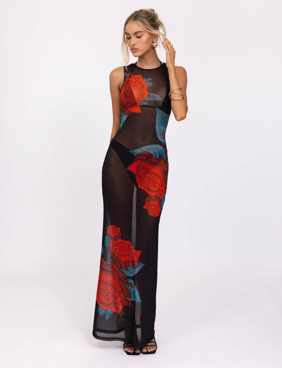 A woman poses in the TIGERMIST JOZIE THREE PIECE DRESS - BLACK : MACRO ROSE - RED ROSE. She pairs the dress with black high heels and wears gold hoop earrings along with a gold bracelet. Her hair is styled in a relaxed updo.