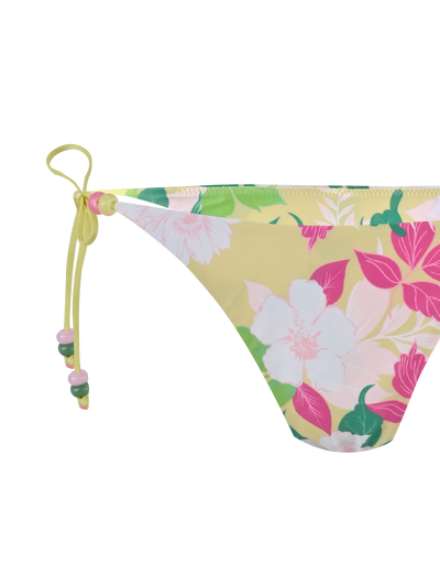 A close-up of the TIGERMIST FINLEA BIKINI BOTTOM - PAISLEY BORDER featuring a yellow floral print, cheeky cut, side tie with bow, and beaded accents.
